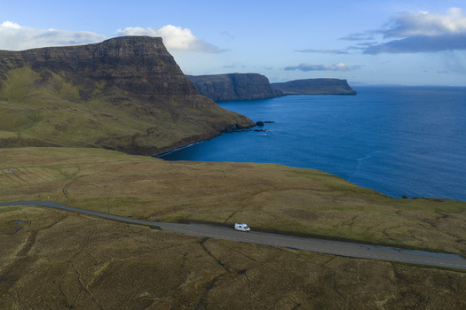 Aerial view of a white camper van driving on a coastal road near the dramatic cliffs of Neist Point Isle of Skye Scotland United Kingdom. Aerial view of a white camper van driving on a coastal road near the dramatic cliffs of Neist Point Isle of Skye Scotland United Kingdom.
