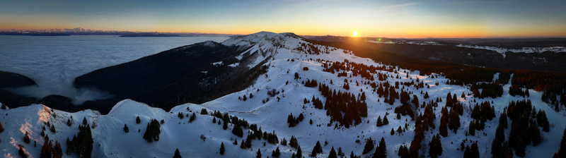 Aerial view of Col de la Faucille with snow covered mountain ridges and pine trees above a sea of clouds at sunset Gex Auvergne Rhone Alpes France. Aerial view of Col de la Faucille with snow covered mountain ridges and pine trees above a sea of clouds at sunset Gex Auvergne Rhone Alpes France.