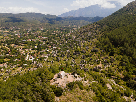 Aerial view of the historic ghost village of Kayakoy with its stone ruins nestled among lush green hills and pine forests in Fethiye Mugla Turkiye. Aerial view of the historic ghost village of Kayakoy with its stone ruins nestled among lush green hills and pine forests in Fethiye Mugla Turkiye.
