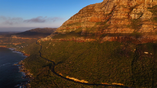 Aerial view of the winding Chapman s Peak Drive along steep rocky cliffs and lush green slopes during golden hour Cape Town Western Cape South Africa. Aerial view of the winding Chapman s Peak Drive along steep rocky cliffs and lush green slopes during golden hour Cape Town Western Cape South Africa.