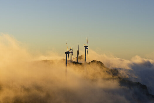 Aerial view of wind turbines on the ridge of Bica da Cana peak rising above a sea of clouds during golden hour in Funchal Madeira Portugal.