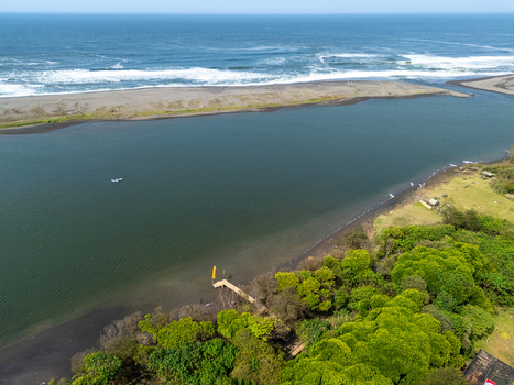 Aerial view of Depok Beach where the river meets the ocean featuring a wooden pier lush green vegetation and sandy coastline in Special Region of Yogyakarta Indonesia. Aerial view of Depok Beach where the river meets the ocean featuring a wooden pier lush green vegetation and sandy coastline in Special Region of Yogyakarta Indonesia.