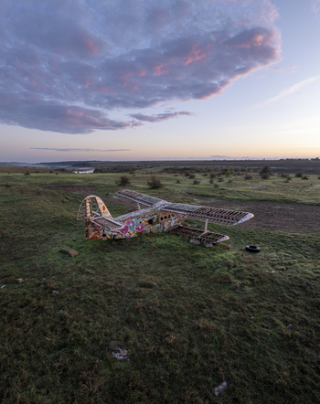 Aerial view of an abandoned graffiti covered biplane resting in a grassy field under a soft sunset sky in Bulgaria. Aerial view of an abandoned graffiti covered biplane resting in a grassy field under a soft sunset sky in Bulgaria.