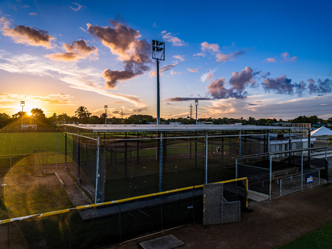 Aerial view of Quality Baseball Academy featuring batting cages and stadium lights on a green field during a vibrant sunset in San Antonio de Guerra Santo Domingo Provinc Dominican Republic. Aerial view of Quality Baseball Academy featuring batting cages and stadium lights on a green field during a vibrant sunset in San Antonio de Guerra Santo Domingo Provinc Dominican Republic.