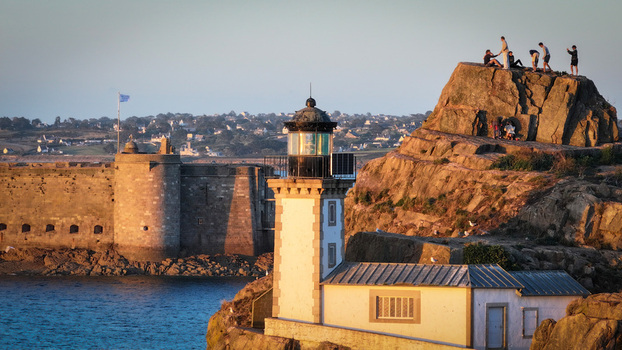 Aerial view of the stark white Ile Louet lighthouse against the rugged sun kissed rocks where figures gather contrasting with the serene blue sea Plouezoc h Bretagne France. Aerial view of the stark white Ile Louet lighthouse against the rugged sun kissed rocks where figures gather contrasting with the serene blue sea Plouezoc h Bretagne France.