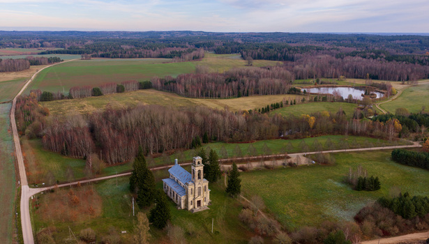 Aerial view of the historic Palendriai church surrounded by lush green fields autumn forests and a small pond in Palendriai Siauliu apskritis Lithuania.