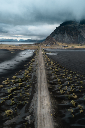 Aerial view of Vestrahorn mountain and a road cutting through black sand dunes under a dramatic cloudy sky in Sveitarfelagid Hornafjordur Iceland. Aerial view of Vestrahorn mountain and a road cutting through black sand dunes under a dramatic cloudy sky in Sveitarfelagid Hornafjordur Iceland.