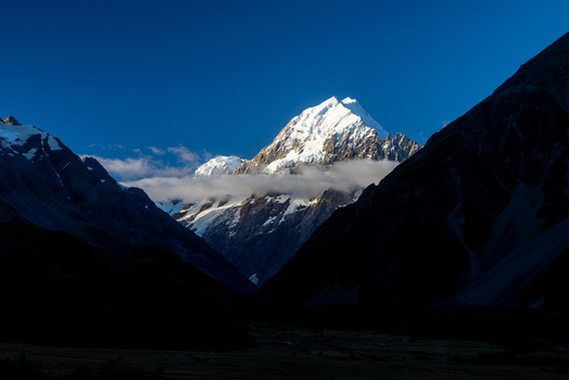 View of the snow capped peak piercing through a sea of clouds embraced by the stark shadows of towering mountains Mount Cook Canterbury Region New Zealand. View of the snow capped peak piercing through a sea of clouds embraced by the stark shadows of towering mountains Mount Cook Canterbury Region New Zealand.