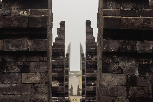 View of the symmetrical stone gates of Cetho Temple with dark weathered blocks leading into a misty background in Kecamatan Jenawi Jawa Tengah Indonesia. View of the symmetrical stone gates of Cetho Temple with dark weathered blocks leading into a misty background in Kecamatan Jenawi Jawa Tengah Indonesia.