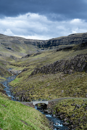 View of the rugged valley of Hvalfjordur with a small stone bridge crossing a stream amidst mossy hills and rocky slopes under a cloudy sky Iceland. View of the rugged valley of Hvalfjordur with a small stone bridge crossing a stream amidst mossy hills and rocky slopes under a cloudy sky Iceland.