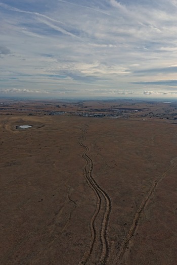Aerial view of winding tire tracks through a vast arid landscape with a small pond under a cloudy sky in Golden Colorado United States.