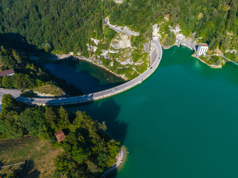 Aerial view of Barrage de Rossens dam curving across the turquoise waters of Lac de la Gruyere surrounded by lush green forests and hills in Pont la Ville Fribourg Switzerland.