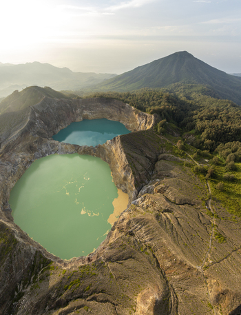 Aerial view of Kelimutu National Park featuring its iconic multi colored volcanic crater lakes surrounded by rugged terrain and lush vegetation in Detusoko East Nusa Tenggara Indonesia.