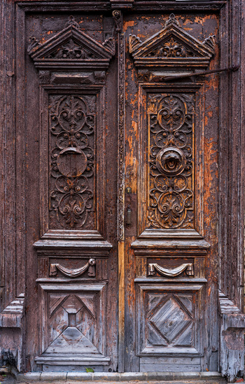 View of an ornate weathered wooden double door featuring intricate carvings and metal knockers in the historic district of Vilnius Vilnius County Lithuania. View of an ornate weathered wooden double door featuring intricate carvings and metal knockers in the historic district of Vilnius Vilnius County Lithuania.