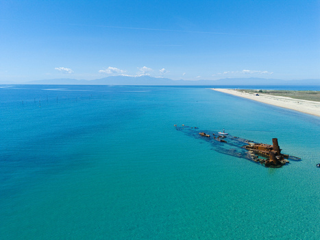Aerial view of the rusty Shipwreck Epanomi resting in turquoise waters along a sandy beach under a clear blue sky Epanomi Greece.