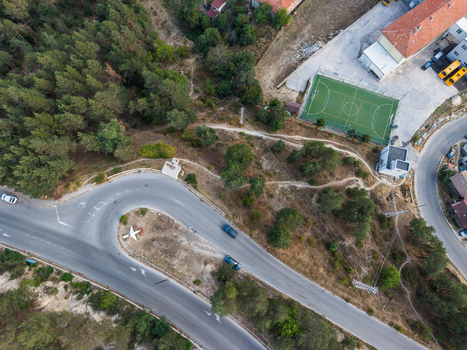Aerial view of a sharp road curve featuring a small airplane monument surrounded by a forest a sports field and buildings in Sveta Petka Pazardzhik Bulgaria. Aerial view of a sharp road curve featuring a small airplane monument surrounded by a forest a sports field and buildings in Sveta Petka Pazardzhik Bulgaria.