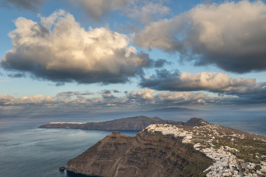 Aerial view of white buildings cascade down rugged cliffs into the deep blue sea a dramatic contrast under a sky full of billowing clouds Fira Thira Greece. Aerial view of white buildings cascade down rugged cliffs into the deep blue sea a dramatic contrast under a sky full of billowing clouds Fira Thira Greece.