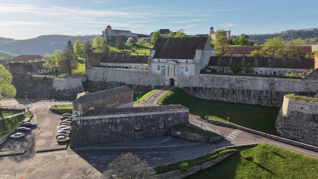 Aerial view of the historic Besancon Citadel featuring massive stone fortifications a central gatehouse and lush green slopes under a clear sky in Besancon Bourgogne Franche Comte France. Aerial view of the historic Besancon Citadel featuring massive stone fortifications a central gatehouse and lush green slopes under a clear sky in Besancon Bourgogne Franche Comte France.