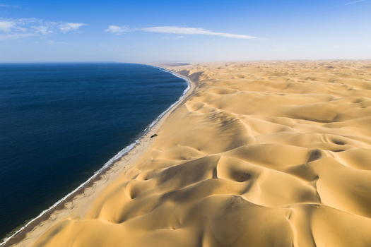 Aerial view of dramatic coastal contrast where the deep blue ocean meets the expansive undulating golden dunes of the Namib Desert Anichab Erongo Namibia. Aerial view of dramatic coastal contrast where the deep blue ocean meets the expansive undulating golden dunes of the Namib Desert Anichab Erongo Namibia.