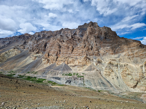 View of Penzi La road winding through the rugged rocky mountain landscape of Zanskar with layered cliffs and sparse green vegetation in Zanskar Ladakh India.