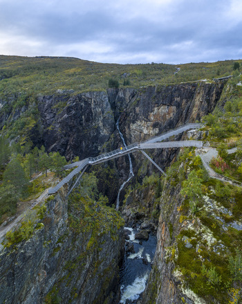 Aerial view of the Voringfossen waterfall and the modern pedestrian bridge spanning the deep rocky canyon in Eidfjord Municipality Vestland Norway.