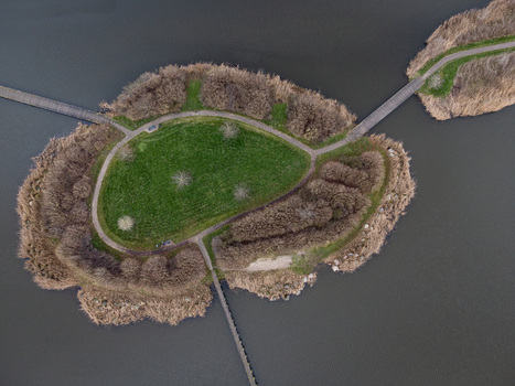 Aerial view of a small island with vibrant green grass surrounded by a ring of brown vegetation and interconnected by pathways standing out against the dark water Overgooi Flevoland Netherlands. Aerial view of a small island with vibrant green grass surrounded by a ring of brown vegetation and interconnected by pathways standing out against the dark water Overgooi Flevoland Netherlands.