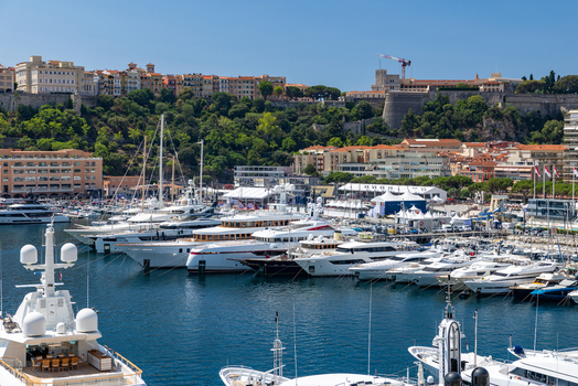 View of Port Hercules filled with luxury yachts and boats against the backdrop of historic buildings and lush hillside in Monaco City Monaco. View of Port Hercules filled with luxury yachts and boats against the backdrop of historic buildings and lush hillside in Monaco City Monaco.