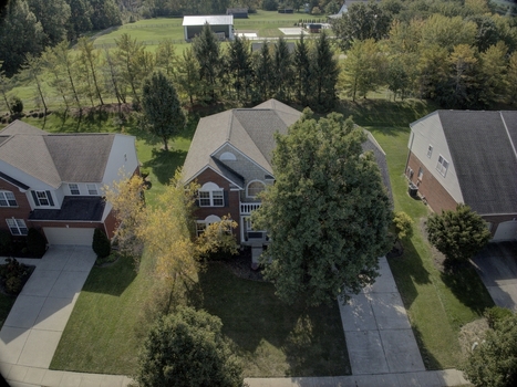 Aerial view of suburban residential houses with brick facades driveways and green lawns surrounded by trees in a neighborhood in Mason Ohio United States.