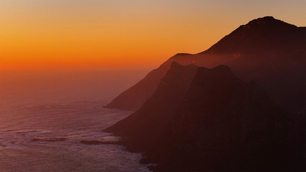 Aerial view of rugged mountain cliffs meeting the Atlantic Ocean under a vibrant orange sunset sky Cape Town Western Cape South Africa. Aerial view of rugged mountain cliffs meeting the Atlantic Ocean under a vibrant orange sunset sky Cape Town Western Cape South Africa.