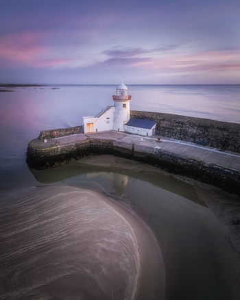 Aerial view of Balbriggan Harbour with its historic lighthouse stone pier and sandy beach at low tide under a soft purple sunset sky in Balbriggan County Dublin Ireland. Aerial view of Balbriggan Harbour with its historic lighthouse stone pier and sandy beach at low tide under a soft purple sunset sky in Balbriggan County Dublin Ireland.
