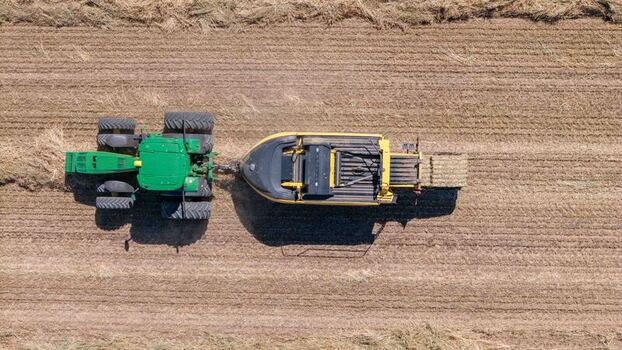 Aerial view of a green tractor pulling a hay baler across a harvested agricultural field in Philadelphia Western Cape South Africa. Aerial view of a green tractor pulling a hay baler across a harvested agricultural field in Philadelphia Western Cape South Africa.
