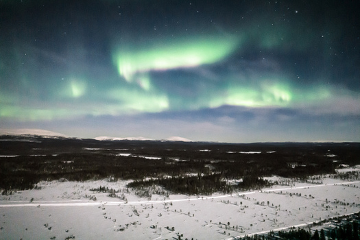 Aerial view of Aurora Borealis illuminating the night sky over the snow covered landscape and forests of Yllasjarvi Lapland Finland.