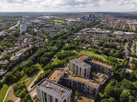 Aerial view of modern apartment buildings with solar panels on rooftops surrounded by lush green spaces and residential neighborhoods in London England United Kingdom. Aerial view of modern apartment buildings with solar panels on rooftops surrounded by lush green spaces and residential neighborhoods in London England United Kingdom.