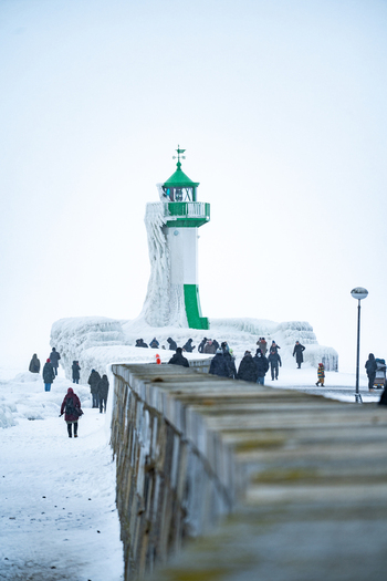 View of Molenfeuer Sassnitz lighthouse covered in thick ice with people walking along the snow covered pier in Sassnitz Mecklenburg Vorpommern Germany.