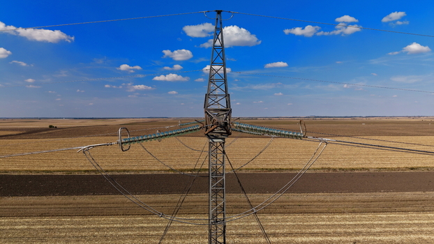 Aerial view of electric power transmission lines spanning across vast agricultural fields under a clear blue sky in Pancevo Serbia.