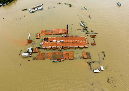 Aerial view of a flooded brick kiln with a tall chimney surrounded by murky floodwaters and small boats in Nabinagar Chittagong Division Bangladesh. Aerial view of a flooded brick kiln with a tall chimney surrounded by murky floodwaters and small boats in Nabinagar Chittagong Division Bangladesh.