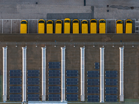 Aerial view of a row of yellow delivery vans parked at a logistics facility with solar panels and ventilation shafts on the roof in Settecamini Lazio Italy.