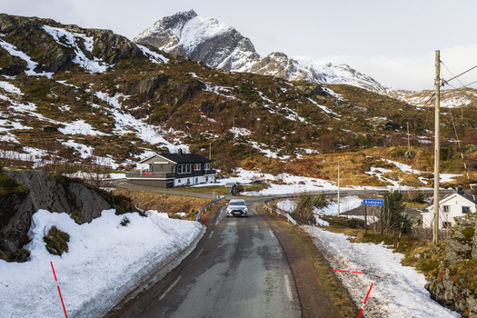 Aerial view of a solitary car driving on a winding asphalt road flanked by melting snow and rugged terrain Kåkernbrua Nordland Norway. Aerial view of a solitary car driving on a winding asphalt road flanked by melting snow and rugged terrain Kåkernbrua Nordland Norway.