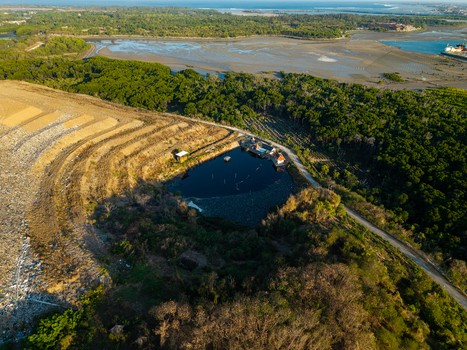 Aerial view of TPA Suwung landfill featuring a dark pond surrounded by dense mangrove forests and coastal terrain in Kecamatan Denpasar Selatan Bali Indonesia.