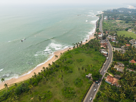 Aerial view of the tropical coastline with a winding road alongside sandy beaches and turquoise ocean waves under an overcast sky in Galle Southern Province Sri Lanka. Aerial view of the tropical coastline with a winding road alongside sandy beaches and turquoise ocean waves under an overcast sky in Galle Southern Province Sri Lanka.