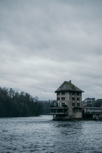 View of a stone building stands firm against the flowing river a testament to history amidst the Rhine Falls Neuhausen am Rheinfall Switzerland. View of a stone building stands firm against the flowing river a testament to history amidst the Rhine Falls Neuhausen am Rheinfall Switzerland.