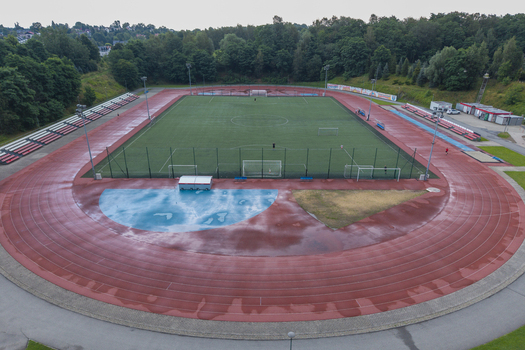 Aerial view of a sports center with a wet running track and soccer field after rain surrounded by lush green trees in Wieliczka Lesser Poland Voivode Poland. Aerial view of a sports center with a wet running track and soccer field after rain surrounded by lush green trees in Wieliczka Lesser Poland Voivode Poland.