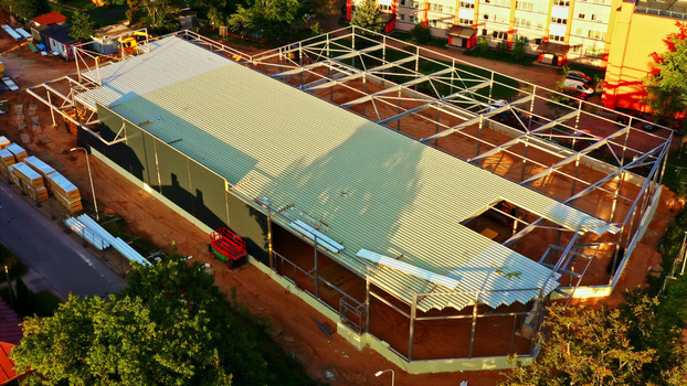 Aerial view of a steel frame construction site for a new building with metal roofing panels and surrounding dirt ground in Latvija. Aerial view of a steel frame construction site for a new building with metal roofing panels and surrounding dirt ground in Latvija.
