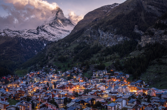 Aerial view of the Matterhorn mountain towering over the illuminated village of Zermatt at dusk with glowing lights in the chalets and surrounding alpine landscape Zermatt Valais Switzerland.