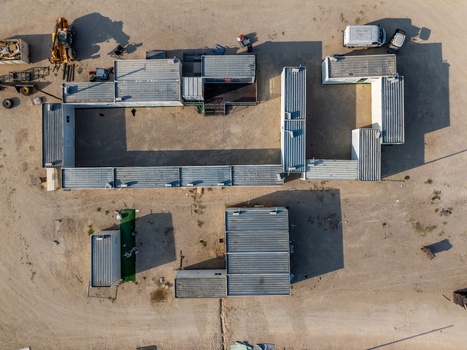 Aerial view of a construction site featuring modular container buildings heavy machinery and dirt ground in Cruz Quebrada Lisboa Portugal.