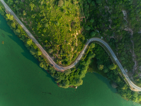 Aerial view of a winding road following the edge of a lush green lake surrounded by dense trees and hills in Udaipur Rajasthan India. Aerial view of a winding road following the edge of a lush green lake surrounded by dense trees and hills in Udaipur Rajasthan India.