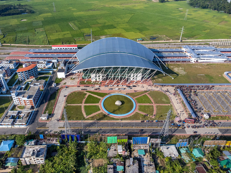 Aerial view of the modern Cox s Bazar Railway Station with its arched roof surrounded by green fields a circular plaza and parking facilities in Cox s Bazar Chittagong Division Bangladesh. Aerial view of the modern Cox s Bazar Railway Station with its arched roof surrounded by green fields a circular plaza and parking facilities in Cox s Bazar Chittagong Division Bangladesh.