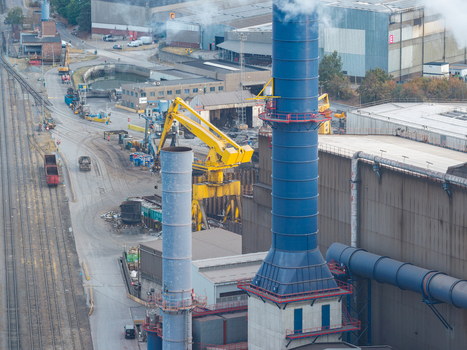 Aerial view of industrial infrastructure at Genk Zuid Rechteroever featuring a blue chimney yellow crane and railway tracks at the steel manufacturing facility in Genk Vlaanderen Belgium. Aerial view of industrial infrastructure at Genk Zuid Rechteroever featuring a blue chimney yellow crane and railway tracks at the steel manufacturing facility in Genk Vlaanderen Belgium.