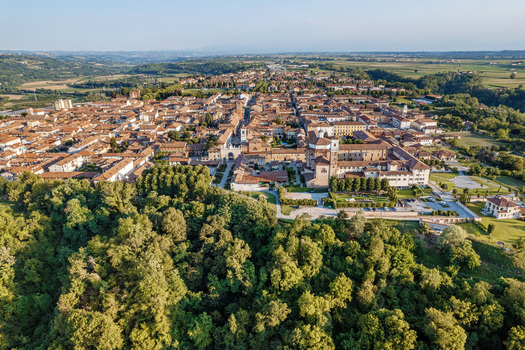 Aerial view of the historic town of Cherasco featuring red tiled rooftops and a large church complex surrounded by lush green trees and rolling hills Cherasco Piedmont Italy. Aerial view of the historic town of Cherasco featuring red tiled rooftops and a large church complex surrounded by lush green trees and rolling hills Cherasco Piedmont Italy.
