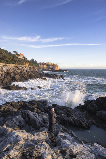 View of the historic village of Tellaro with colorful houses on the coast crashing waves against dark rocks and a man standing on the shore Tellaro Liguria Italy. View of the historic village of Tellaro with colorful houses on the coast crashing waves against dark rocks and a man standing on the shore Tellaro Liguria Italy.